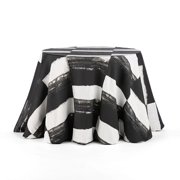 A round table covered with a striking black and white striped tablecloth featuring broad, diagonal brushstroke patterns, available through our Helena Midnight rental service.