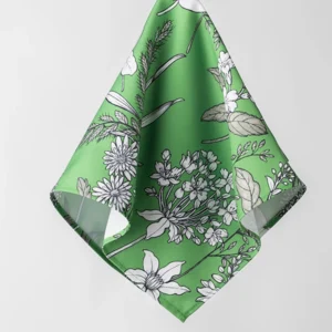 A Dixie Fern Green cloth napkin with a white floral pattern is hanging in front of a plain white background, resembling an elegant example you'd find in a green floral tablecloth rental collection.