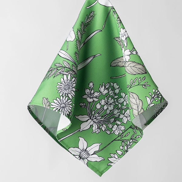 A Dixie Fern Green cloth napkin with a white floral pattern is hanging in front of a plain white background, resembling an elegant example you'd find in a green floral tablecloth rental collection.