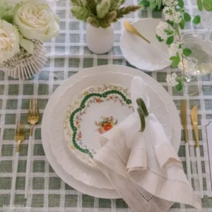 A table setting with green and white plates, decorated with Hemstitch White & Flax Napkin rental.