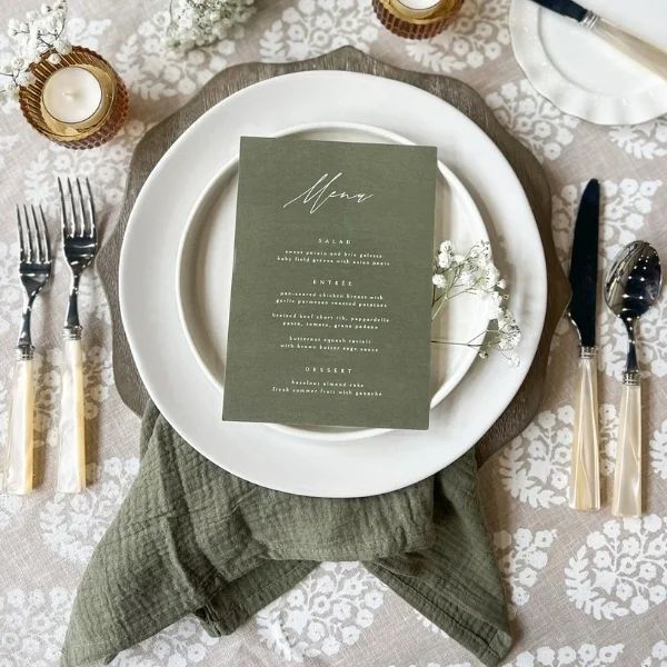 A table setting with a green napkin and Maiie Zinc available for table linen rental.