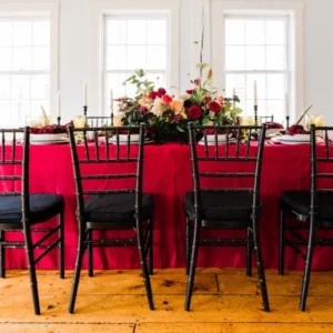 A red Montana Suede Lipstick tablecloth and black chairs in a dining room available for event linen rental.