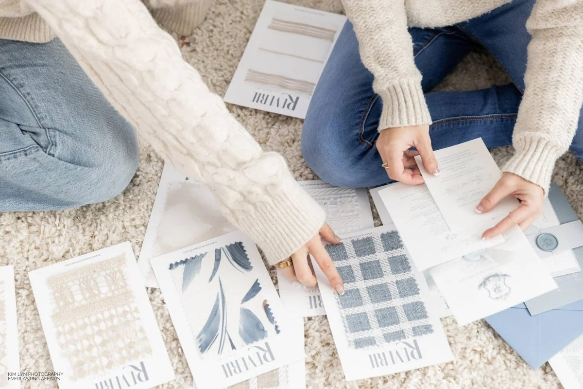 Two women sitting on the floor and looking at paint samples while discussing their upcoming event linen rental.