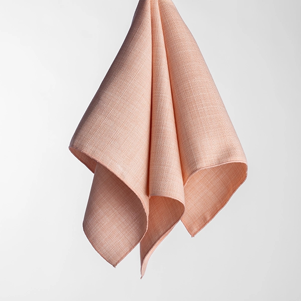 A Nola Apricot fabric napkin hangs with folds, against a plain white background.