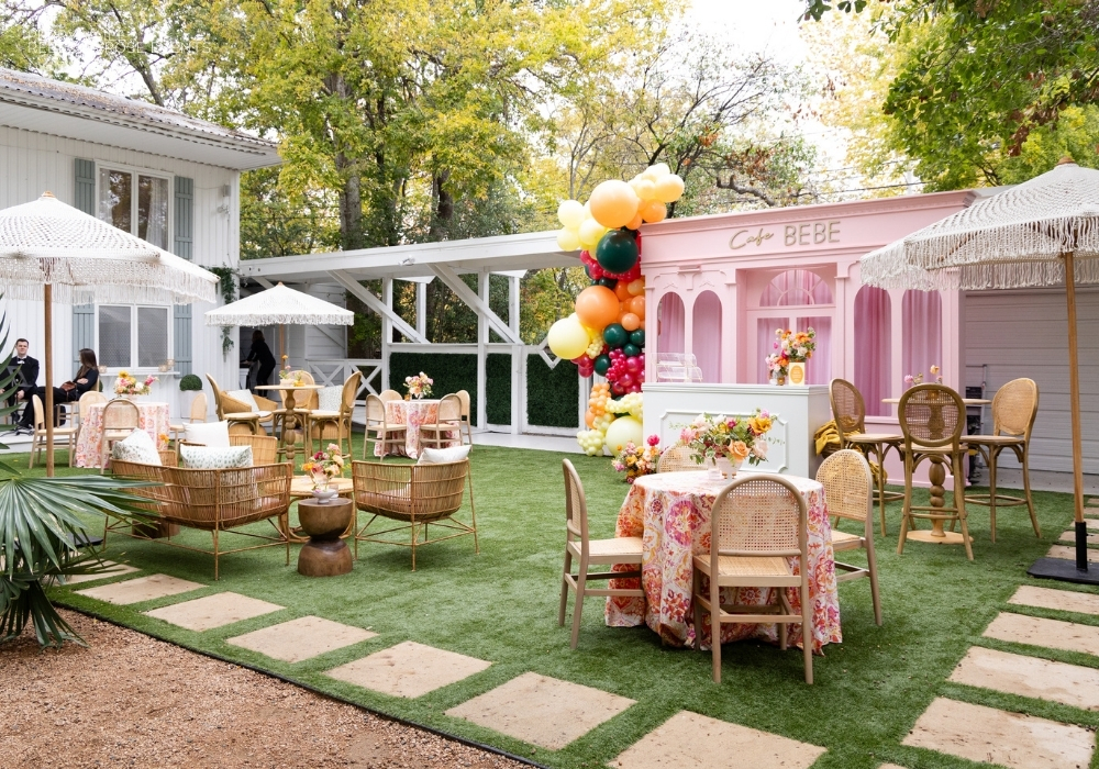 Outdoor event setup with rattan furniture and a pastel-colored balloon arch next to a pink booth signposted "bebe.