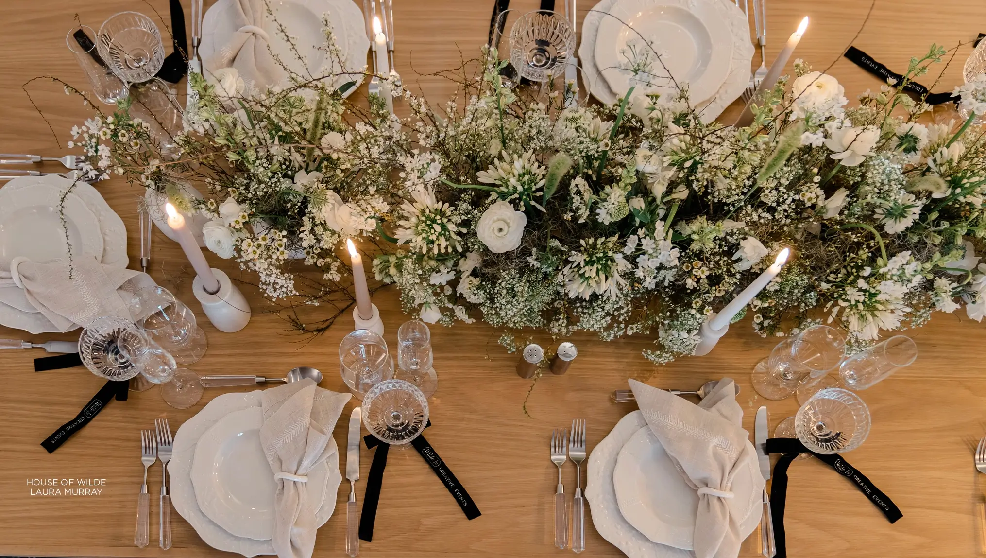 Elegant dining table setting with white florals, candles, and a rustic wooden table for a reverie social gathering.