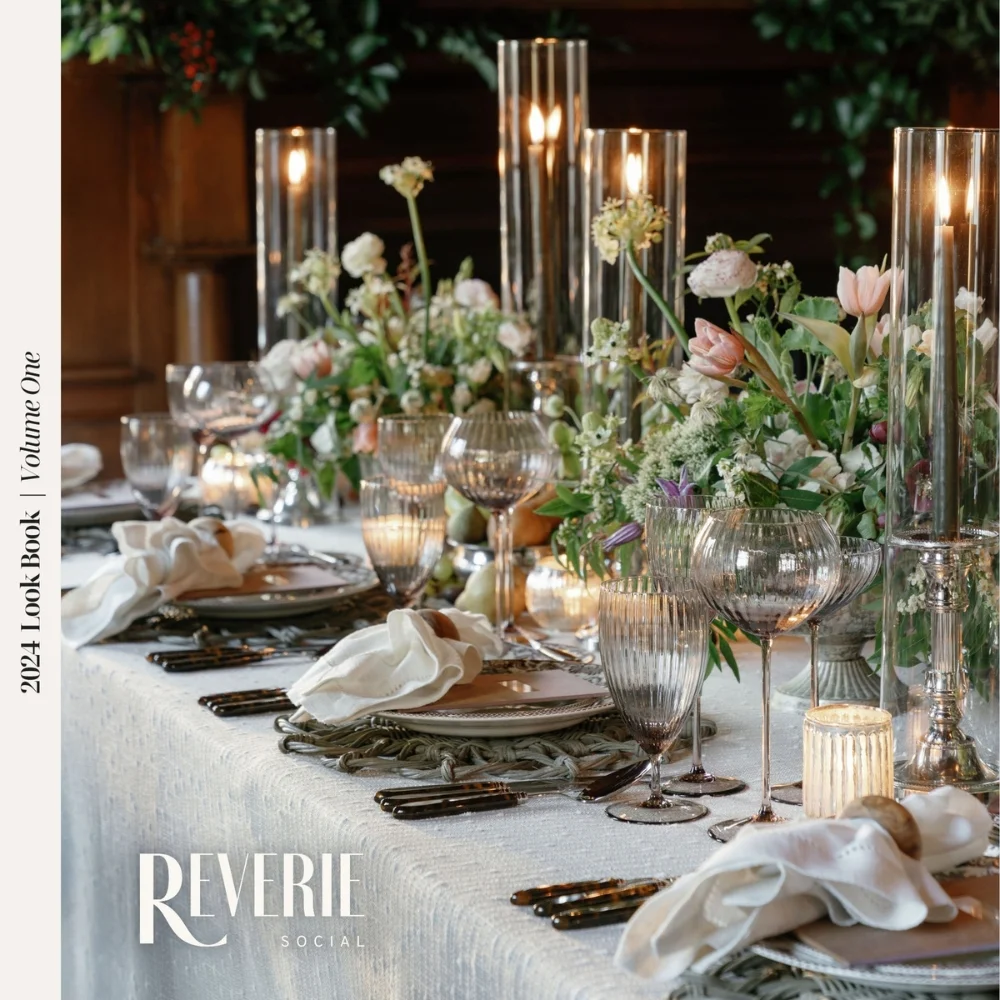 Elegant dining table set for a formal event with glassware, candles, and floral arrangements. Text reads "2024 Look Book | Volume One" and "Reverie Social" on the image.