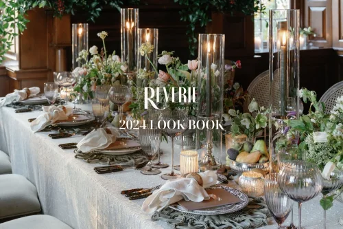 A beautifully set dining table with elegant decorations and floral arrangements for the Reverie 2024 Look Book. Candles, glassware, and place settings create a sophisticated ambiance, complemented by luxurious tablecloths from our linen rental service.