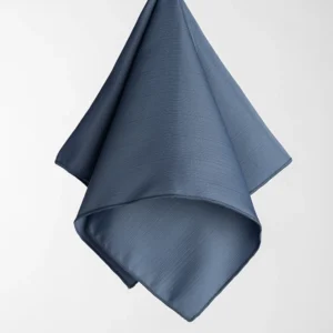 The Monaco Ocean (Copy) handkerchief, featuring a dark blue hue and a subtle textured pattern, is hanging against a plain white background.