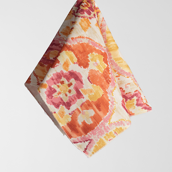 A square piece of cloth with a colorful floral pattern in shades of orange, yellow, and pink, hanging against a plain white background.