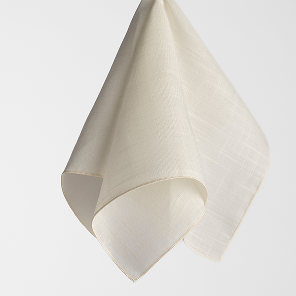 A single, neatly folded, light beige cloth napkin is suspended against a plain white background.