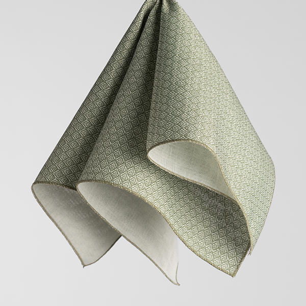 A neatly folded, green-patterned fabric with diamond shapes, draped from an off-frame hook against a plain, light gray background.