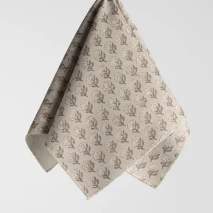 A beige cloth hangs against a plain background, featuring a repeating pattern of small, intricate, dark brown leaves.