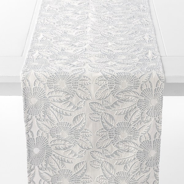 A light-colored table runner with a floral pattern is draped over the center of a white table.