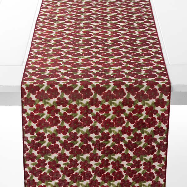 A white table with a runner featuring a pattern of red flowers and green leaves.