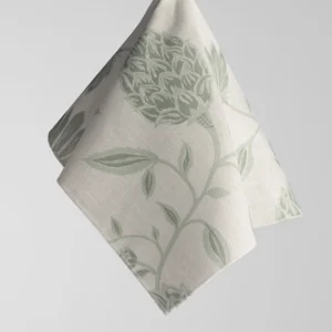 A beige fabric square with a green floral pattern of leaves and petals, hanging diagonally against a light grey background.