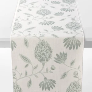 A white table runner with a botanical pattern in light green featuring stylized flowers and leaves draped over a table edge.