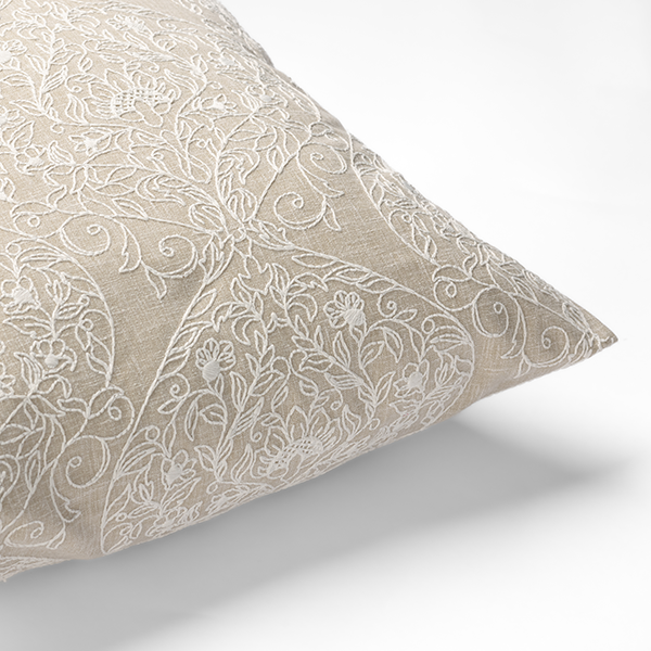 A beige pillow with intricate white floral embroidery is shown against a white background.