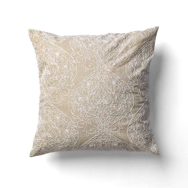 A square beige pillow with intricate white embroidery featuring floral and geometric patterns.