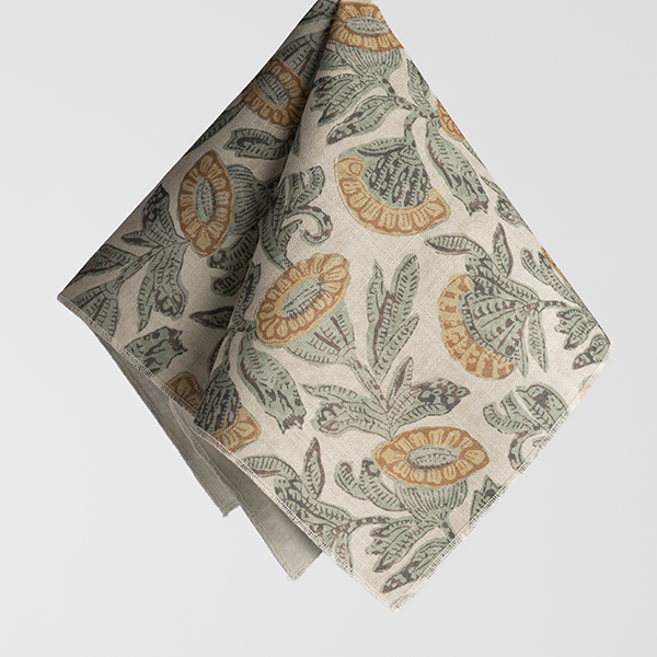 A beige cloth napkin with green leaves and orange flowers printed on it, folded neatly against a plain white background.