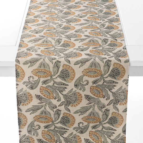 A table runner with a floral pattern featuring gray and orange hues is draped over a white table.