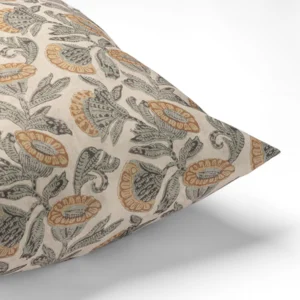 A close-up of a decorative pillow with a floral pattern in green and orange on a beige background.