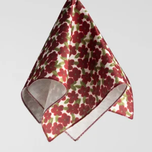 A hanging, floral patterned cloth napkin with red and green flowers on a white background.