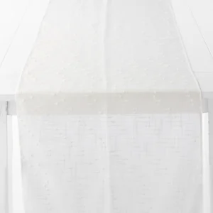 A white, textured table runner with a subtle pattern is draped over the edge of a white table.