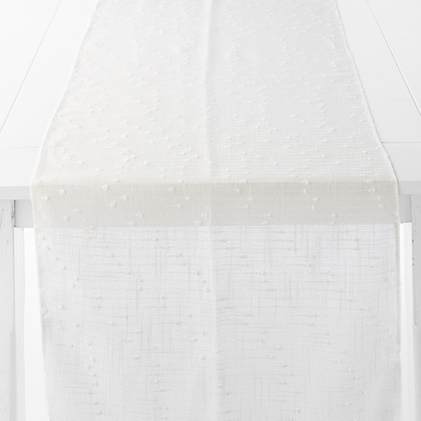 A white, textured table runner with a subtle pattern is draped over the edge of a white table.