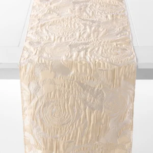 A cream-colored table runner with an elegant, textured floral pattern draped over a white table.