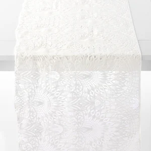 A white lace table runner with an intricate floral pattern is draped over the edge of a table.