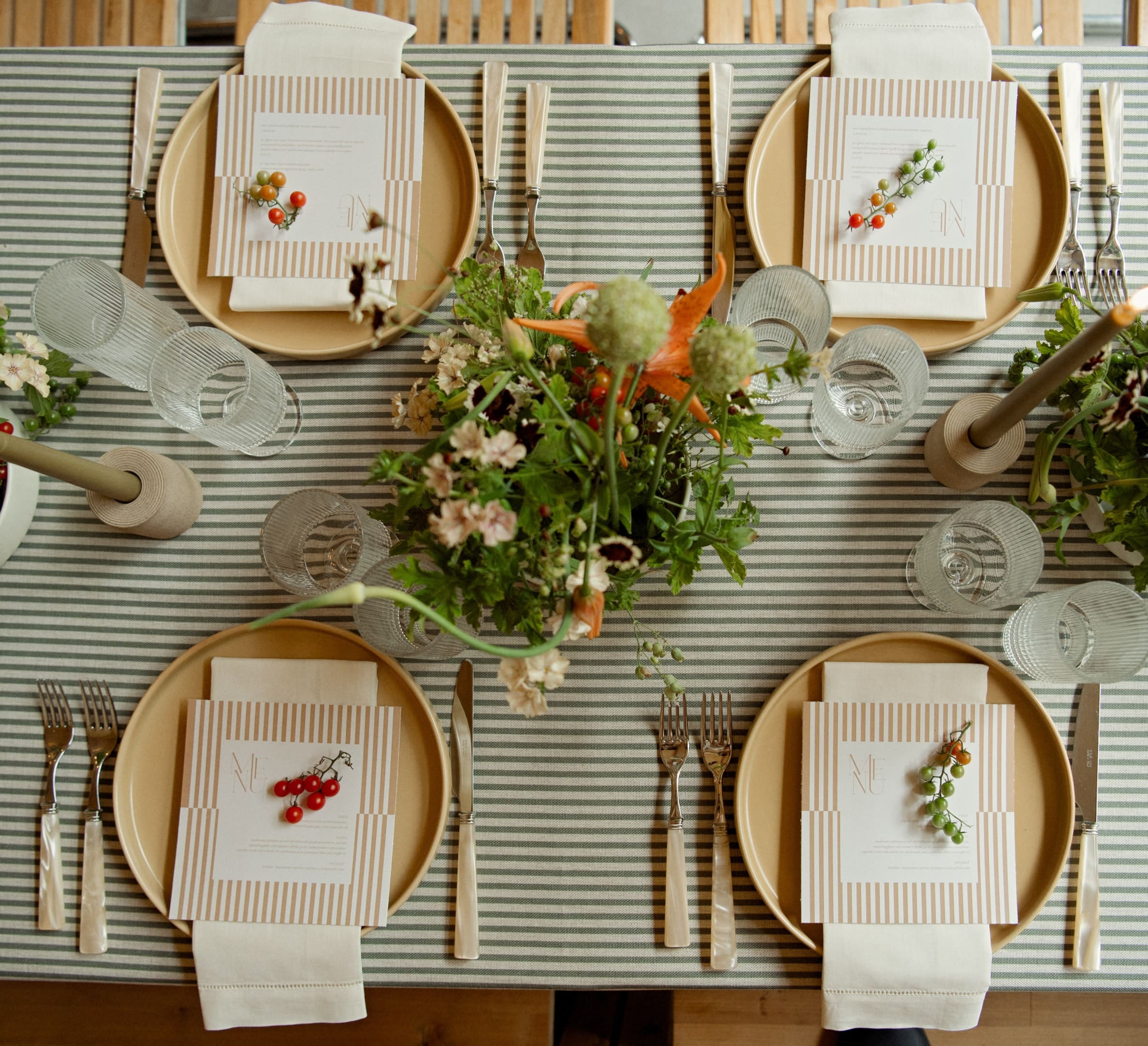 Top-down view of a neatly set dining table with striped tablecloth, yellow plates, napkins, cutlery, glasses, and floral centerpieces.