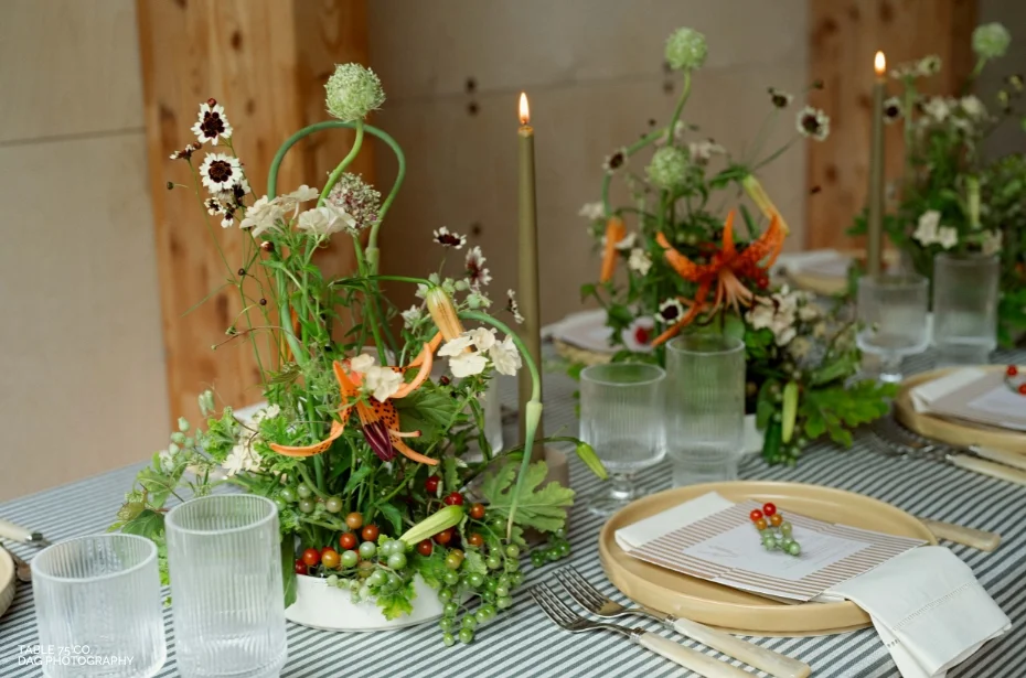 Table setting with lit candles, floral centerpieces, striped tablecloth, and place settings with glassware and cutlery.