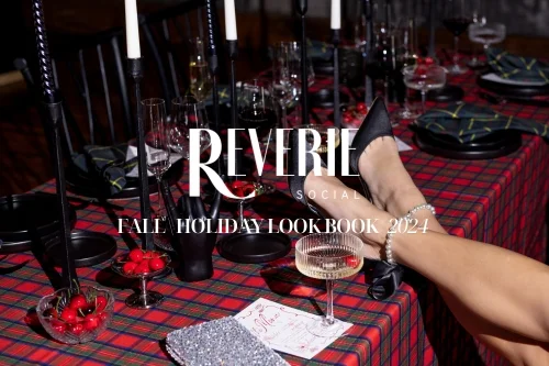 A table featuring a red plaid cloth from our table linen rental service is set with black candlesticks, glasses, and bowls of cherries. A person wearing black shoes rests their legs on the table. Text reads "Reverie Social Fall Holiday Lookbook 2024.