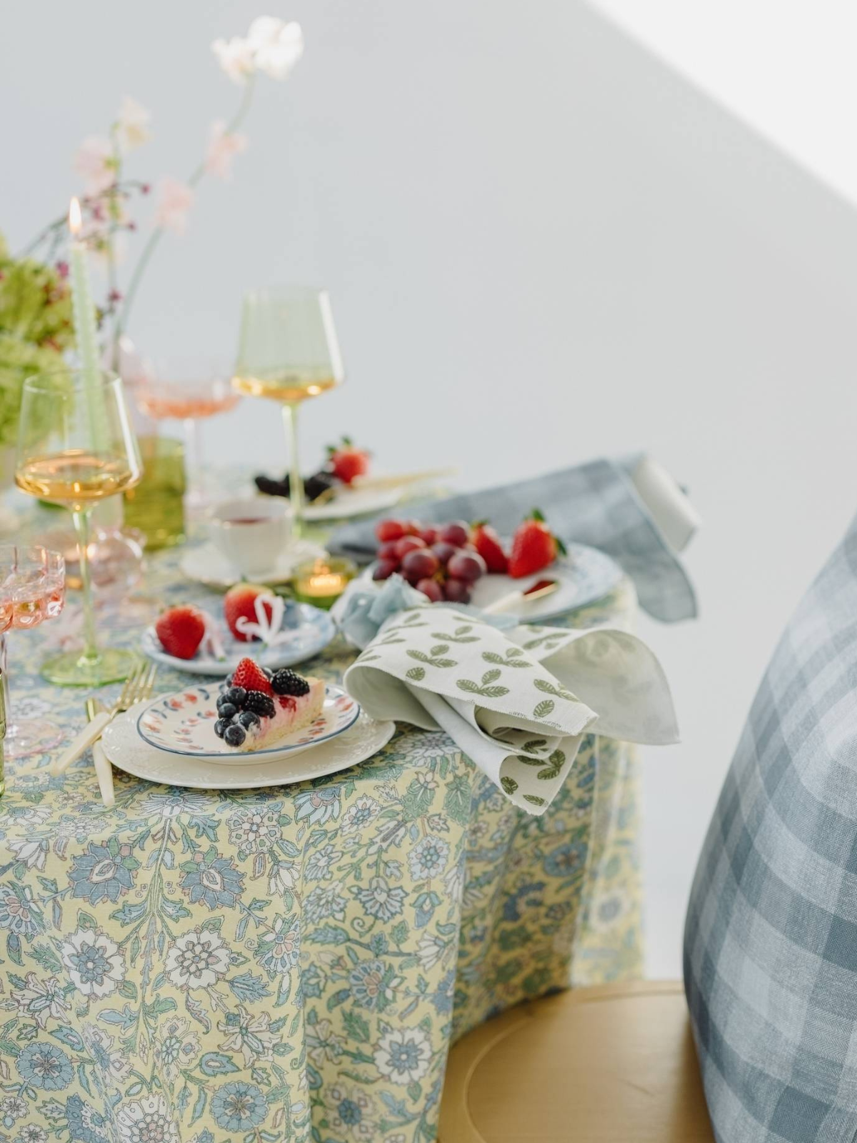 Table set with floral tablecloth, plates of berries, wine glasses, candles, and blue-patterned napkins.